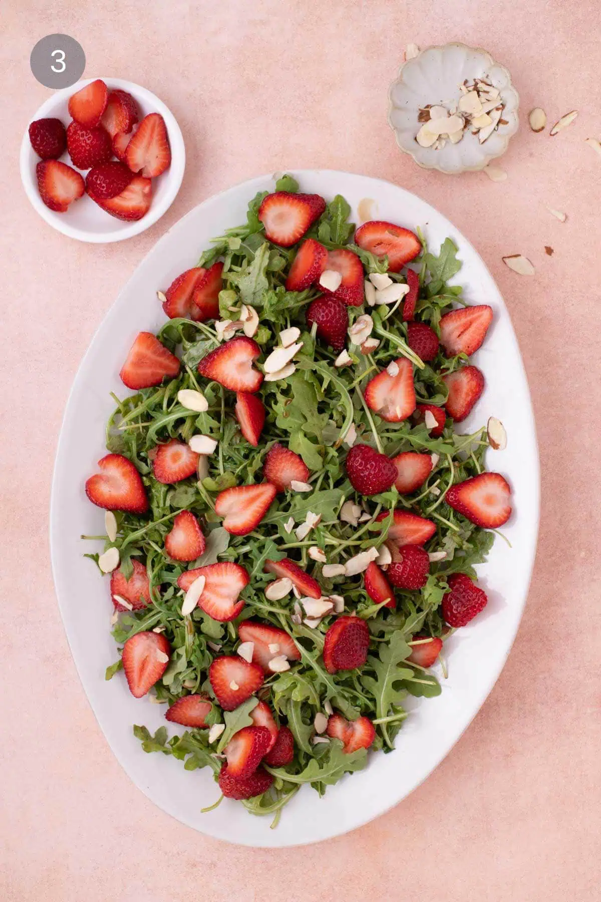Arugula salad arranged on platter with sliced strawberries and almonds