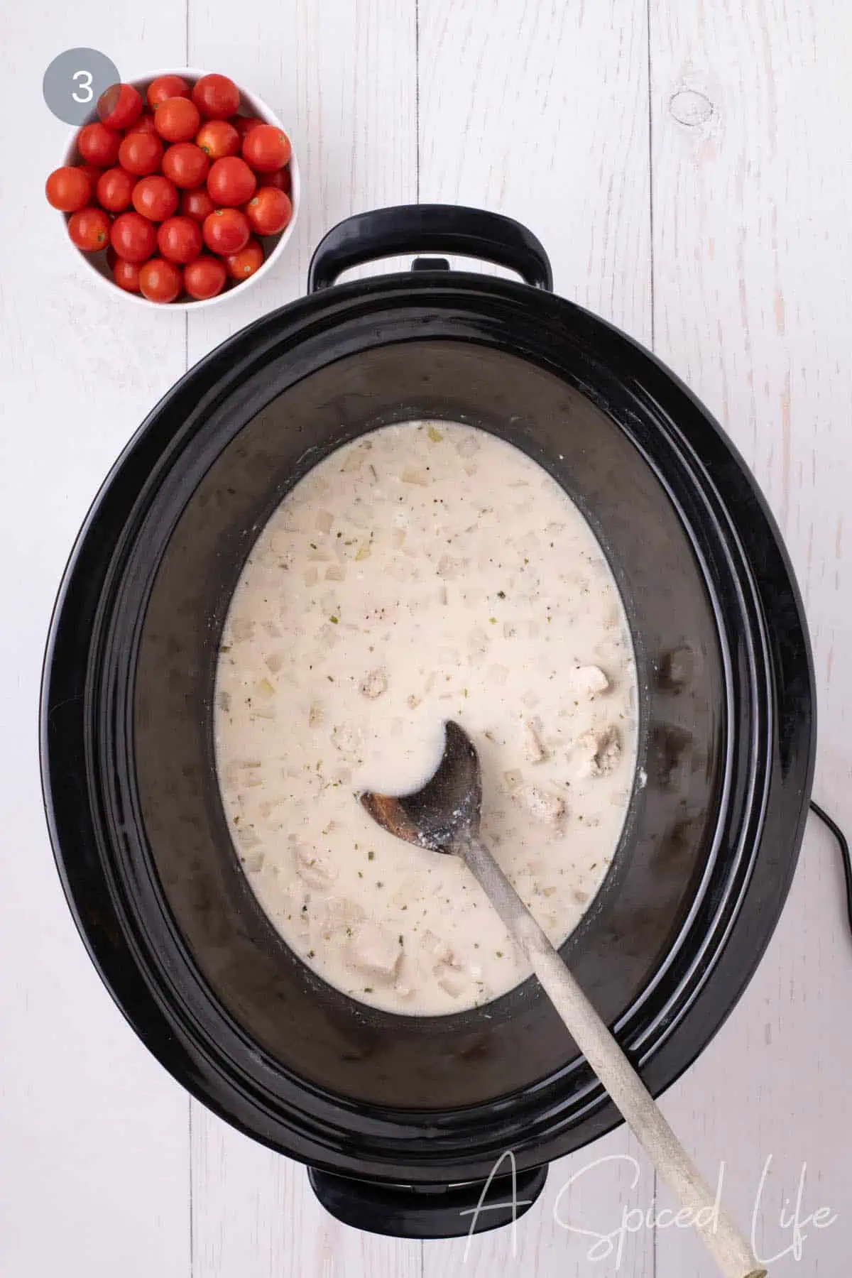 Creamy sauce stirred together with chicken and onion in a slow cooker.