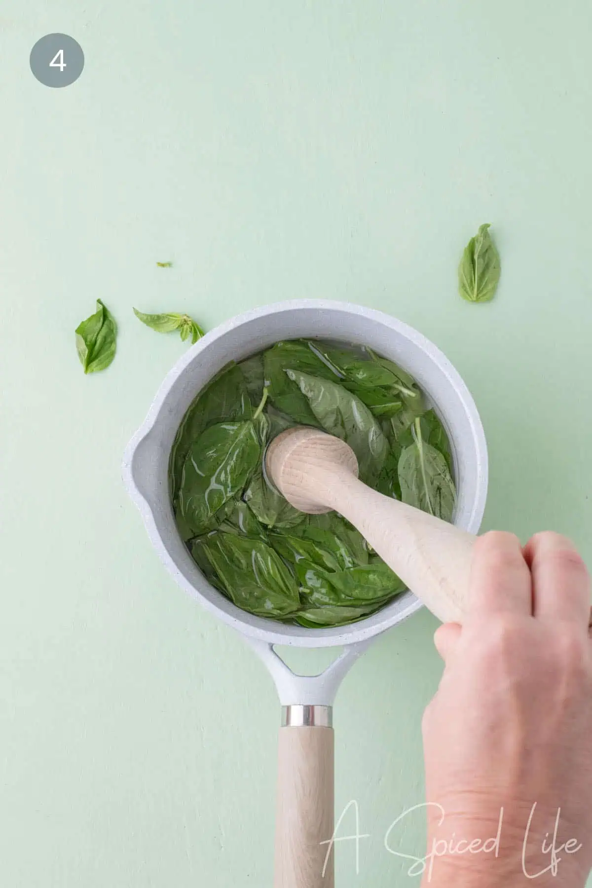 Gently pressing basil leaves to release their oils and let them infuse into the syrup