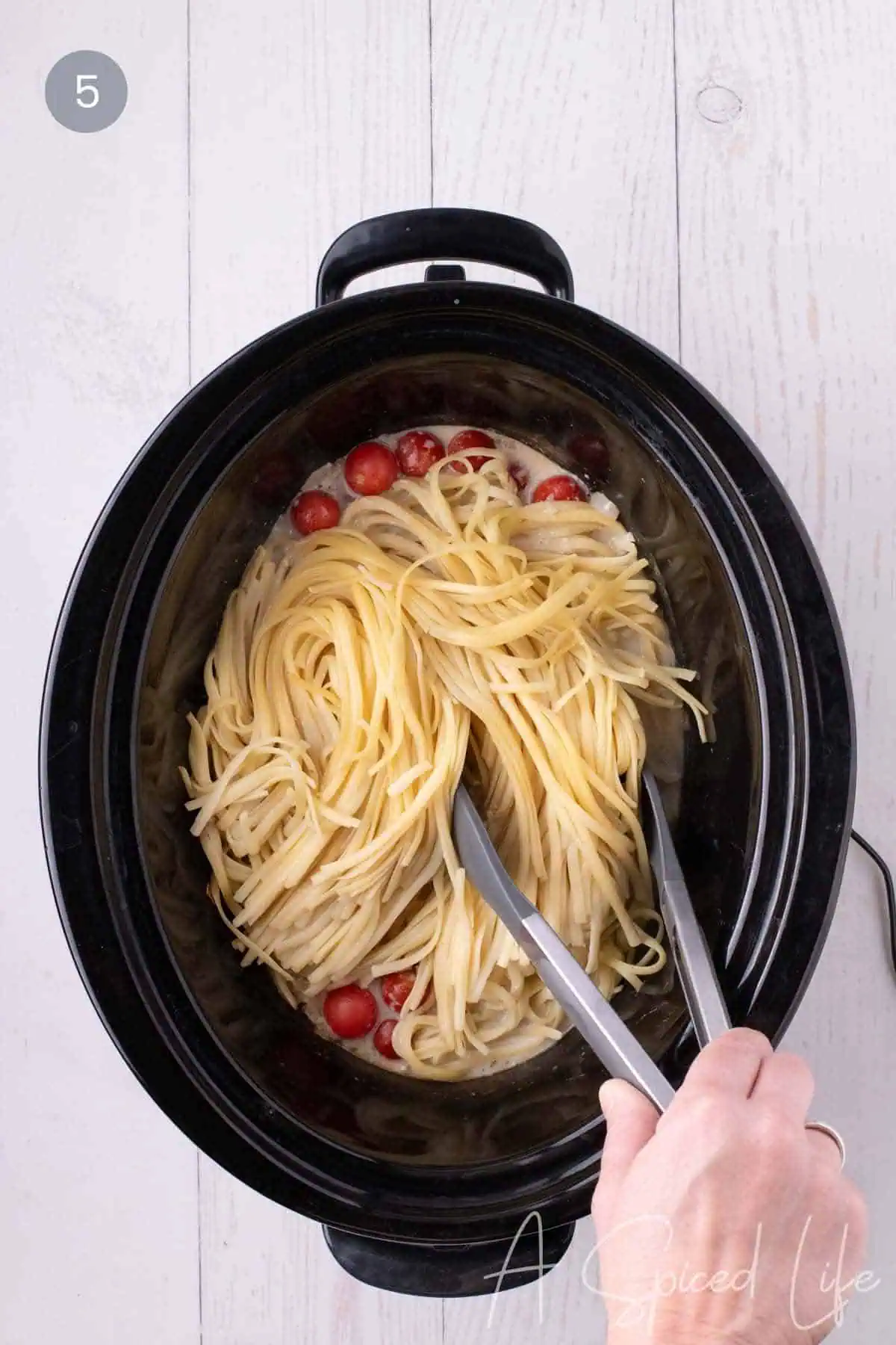 Cooked spaghetti being tossed into creamy chicken sauce in a slow cooker.