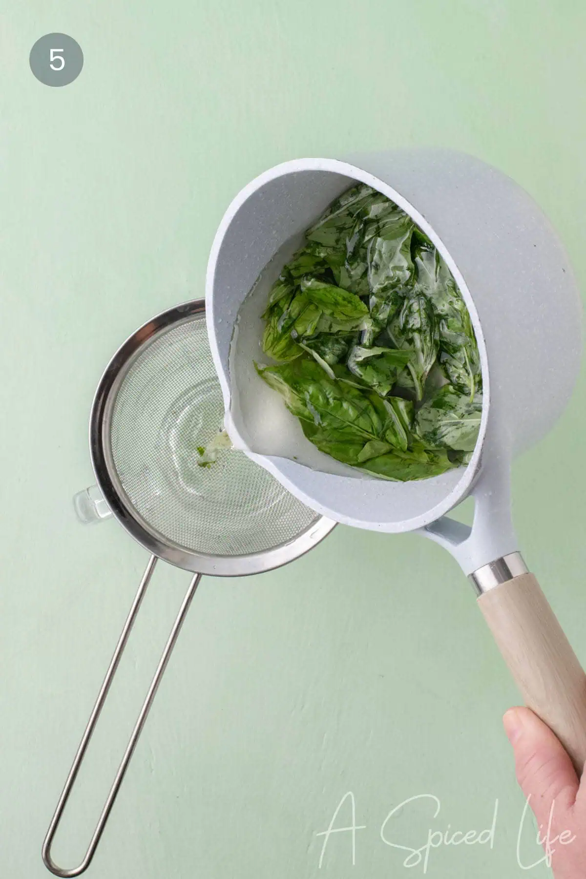 Pouring basil simple syrup through a fine mesh sieve to remove leaves