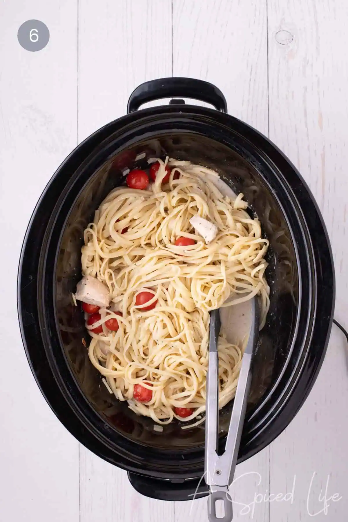 Finished chicken spaghetti tossed with cherry tomatoes in a slow cooker.