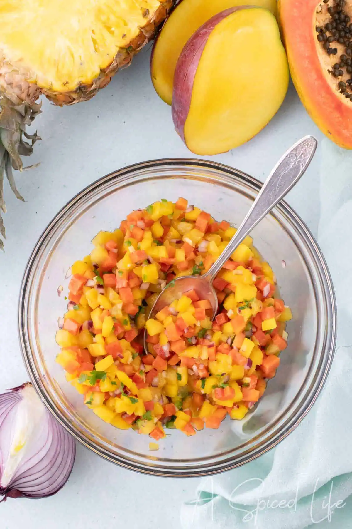 fresh mango papaya salsa with pineapple in a glass bowl with diced fruit and spoon