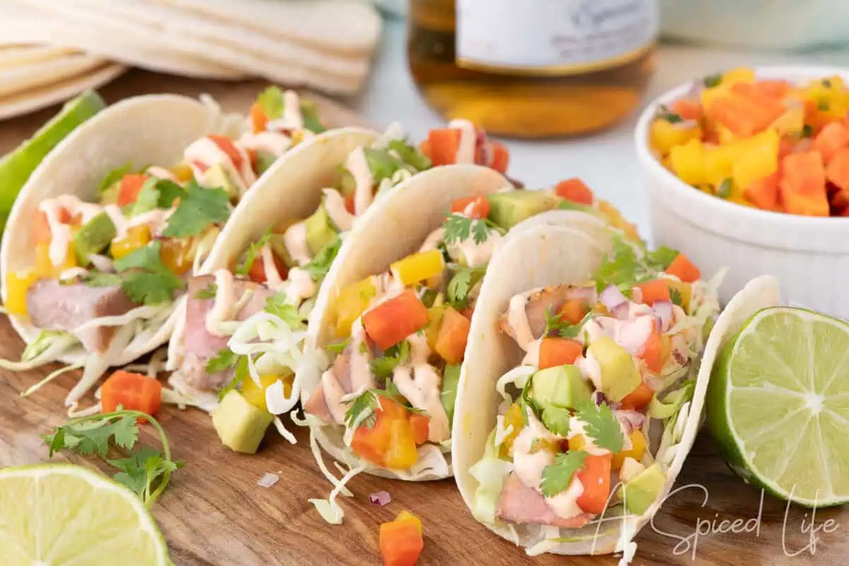 Seared ahi tuna tacos topped with mango papaya salsa, avocado, cabbage, cilantro, and creamy sriracha sauce on corn tortillas