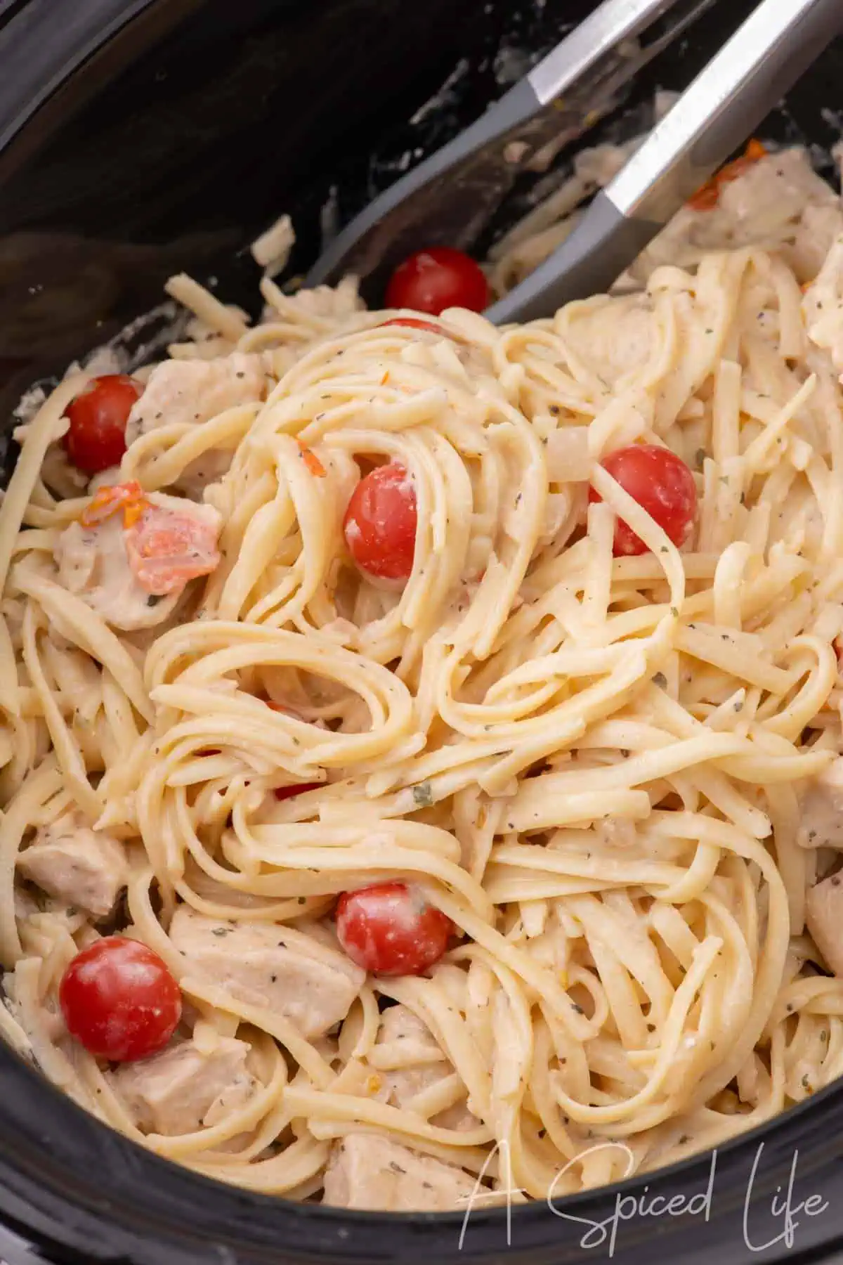Chicken spaghetti being tossed in a slow cooker with creamy sauce and tomatoes