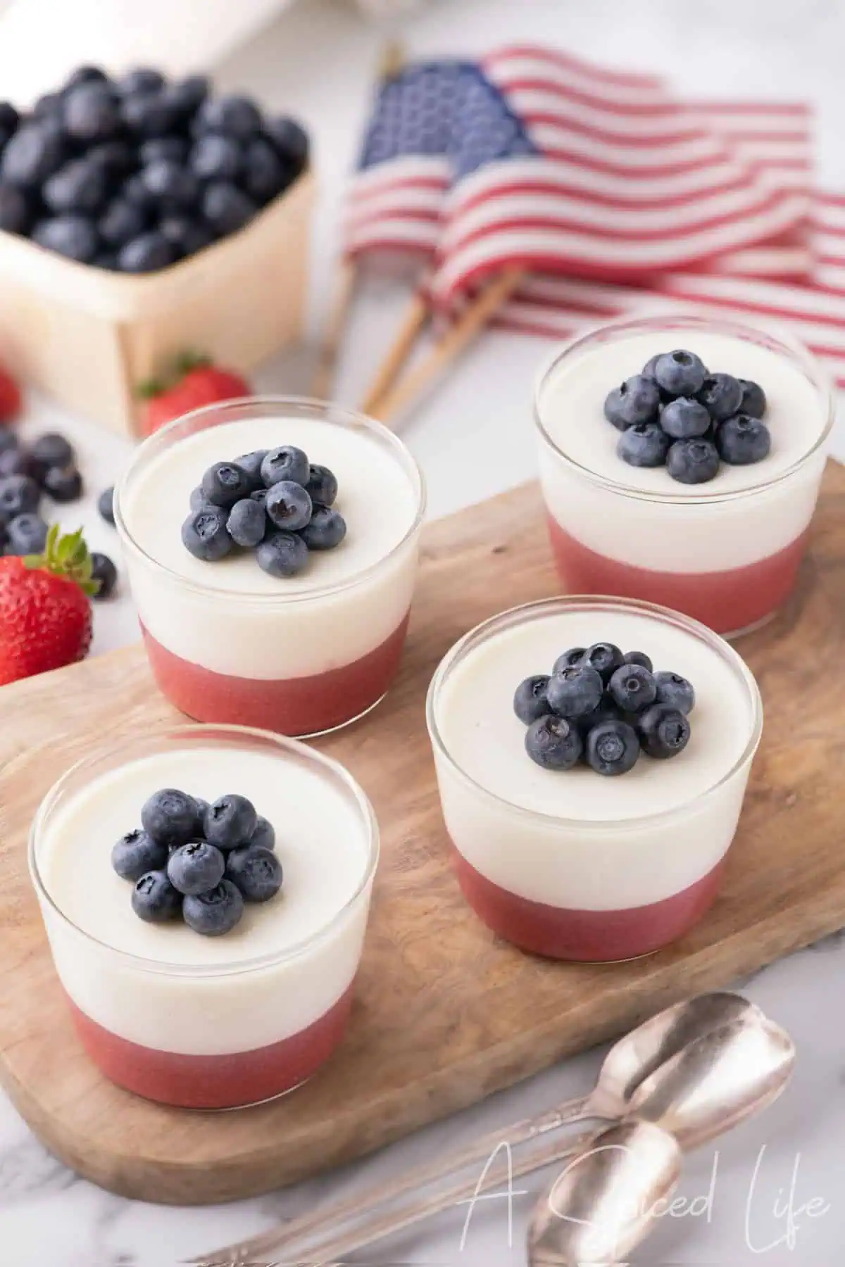 Red white and blue coconut panna cotta desserts topped with blueberries on a serving board.
