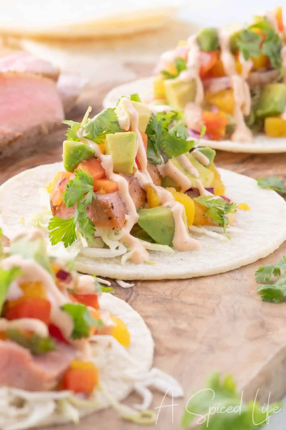 Close-up of seared ahi tuna tacos topped with mango papaya salsa, avocado, cilantro, and creamy sriracha sauce