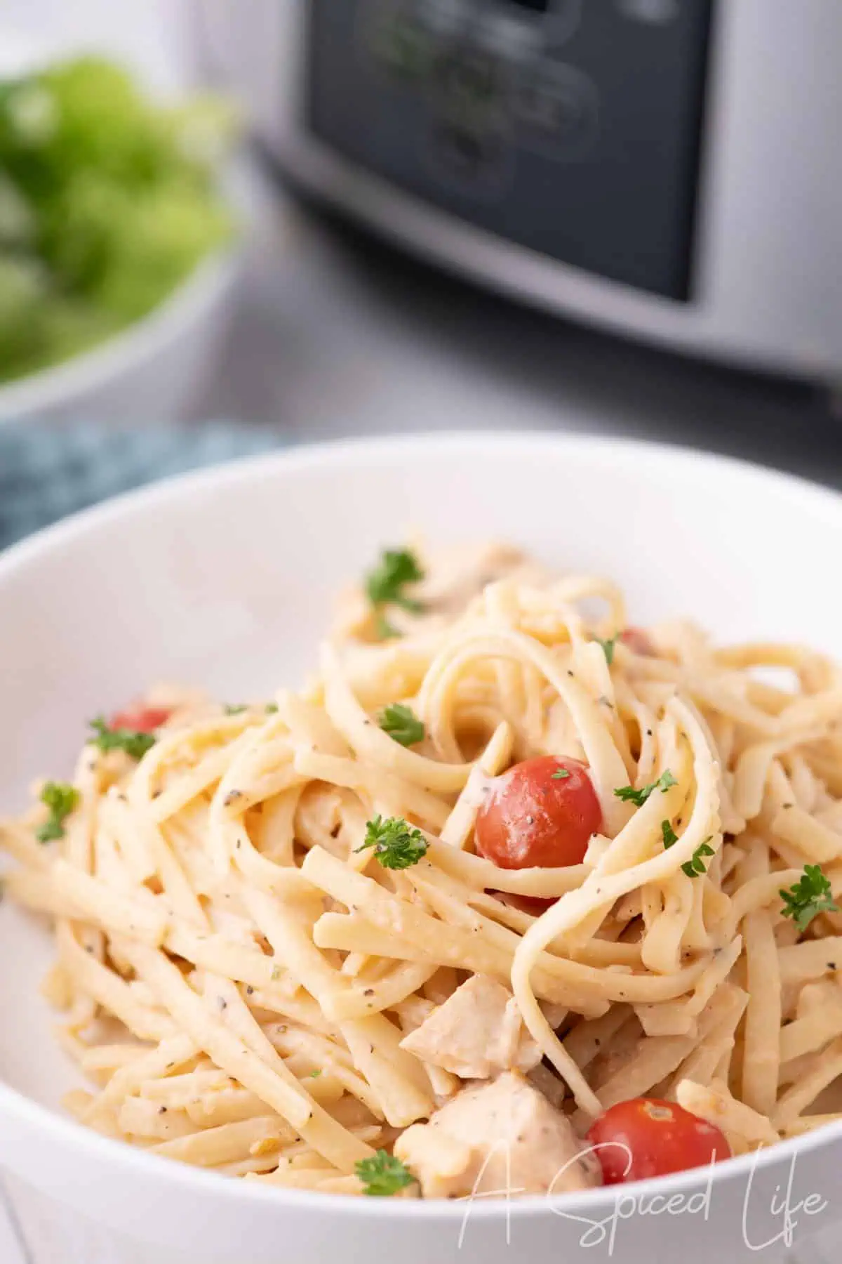 Bowl of creamy chicken spaghetti with parsley and cherry tomatoes