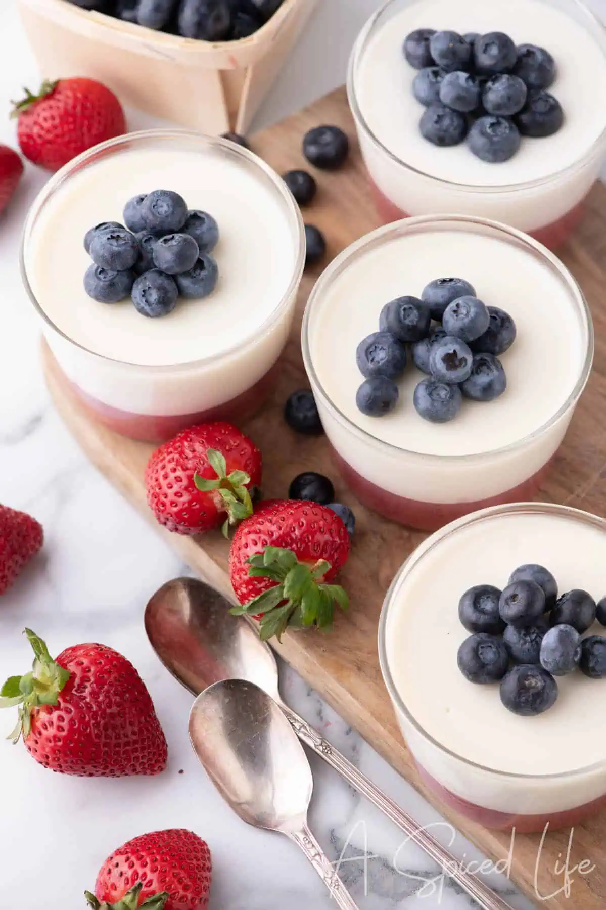 Layered coconut panna cotta cups with strawberries and blueberries on a wooden serving board.