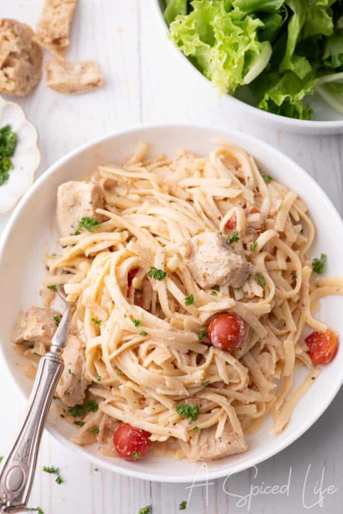 Overhead view of chicken spaghetti in a white bowl with herbs and tomatoes