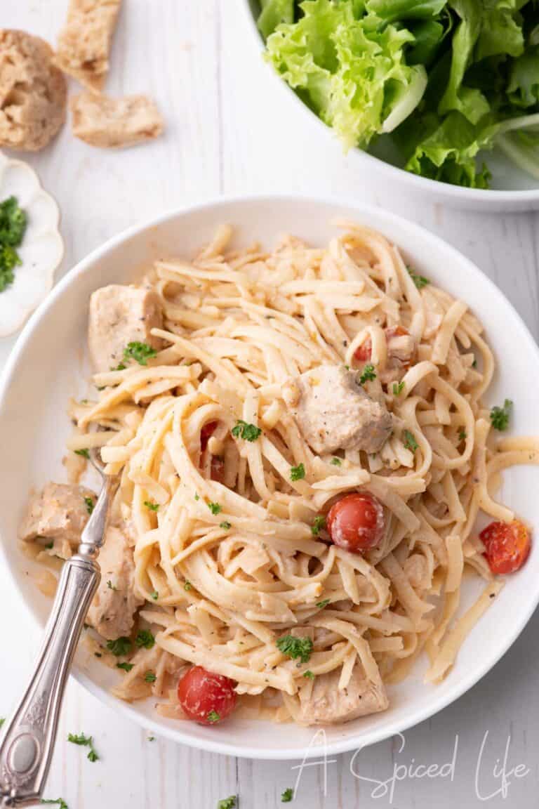 Overhead view of chicken spaghetti in a white bowl with herbs and tomatoes