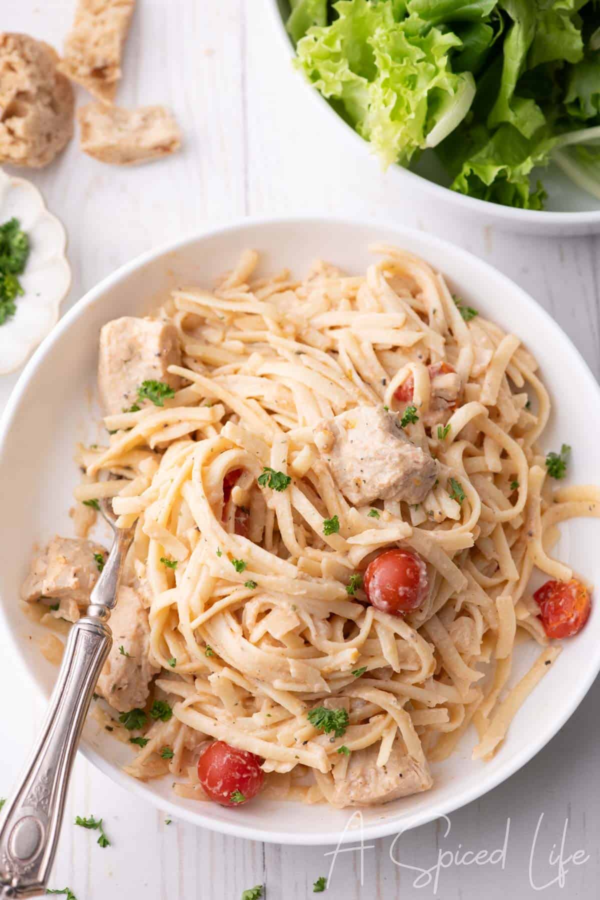 Overhead view of chicken spaghetti in a white bowl with herbs and tomatoes