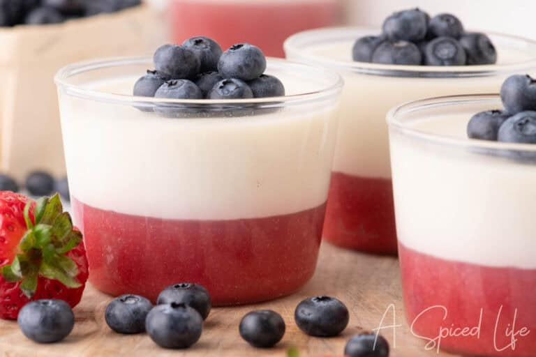 Close-up of coconut panna cotta cups topped with blueberries and layered strawberry puree.