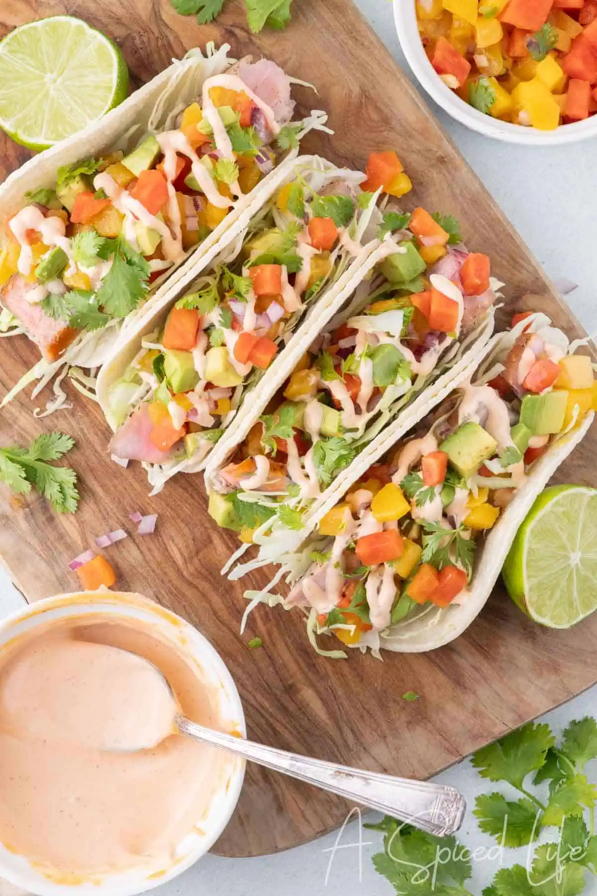 Seared ahi tuna tacos with avocado, mango papaya salsa, cabbage, cilantro, and creamy sriracha sauce