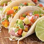 Ahi tuna tacos topped with mango papaya salsa, avocado, cabbage, cilantro, and creamy sriracha sauce beside fresh lime