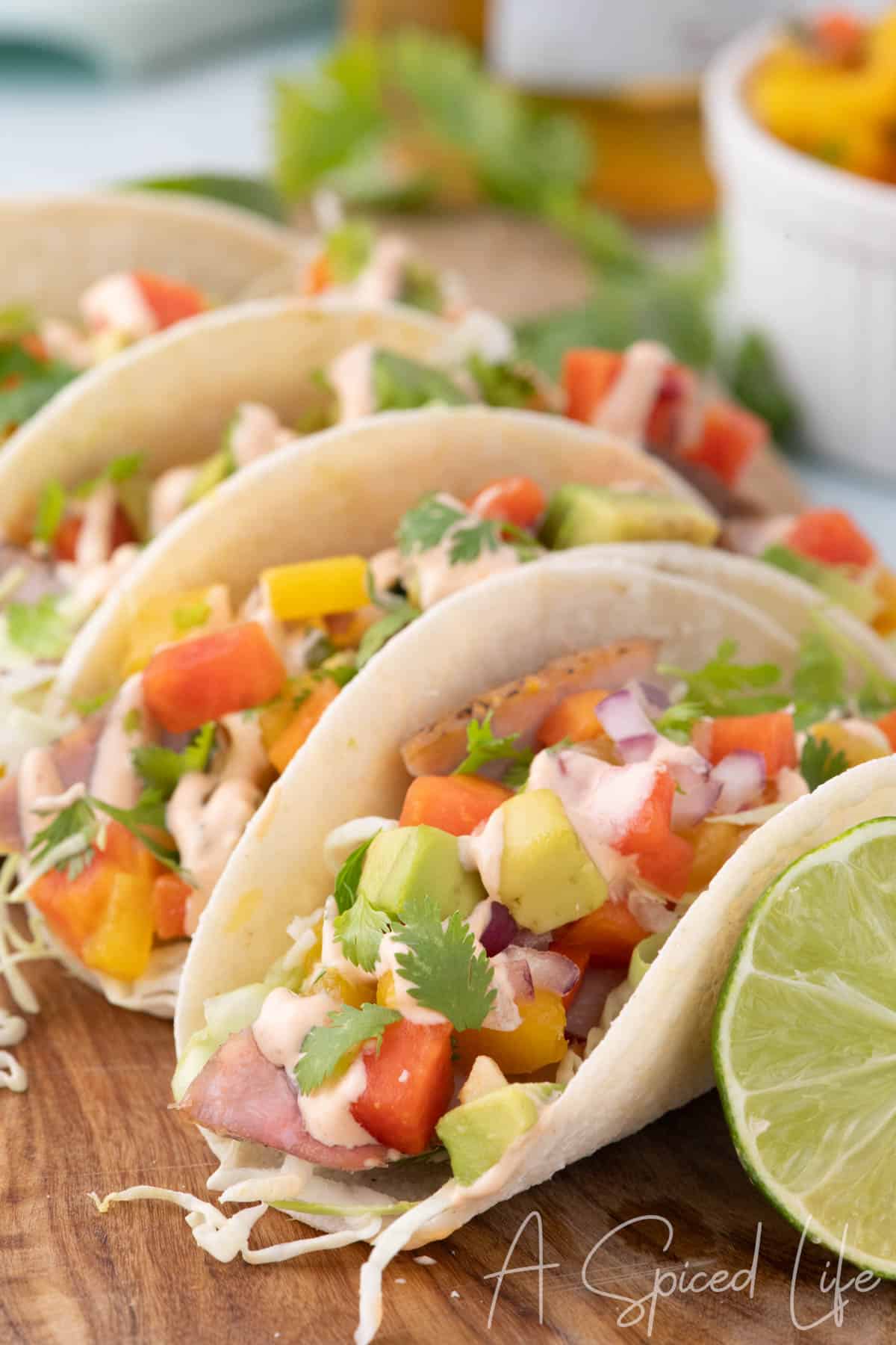 Ahi tuna tacos topped with mango papaya salsa, avocado, cabbage, cilantro, and creamy sriracha sauce beside fresh lime