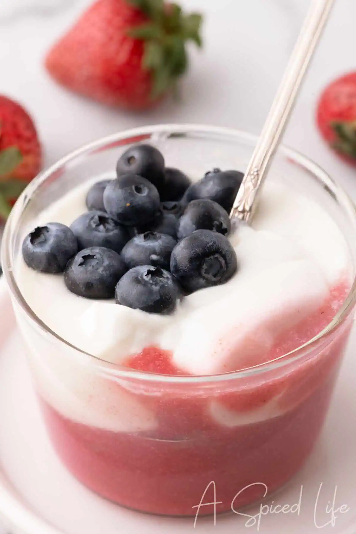 Spoon scooping creamy coconut panna cotta layered with fresh strawberry purée and topped with blueberries.