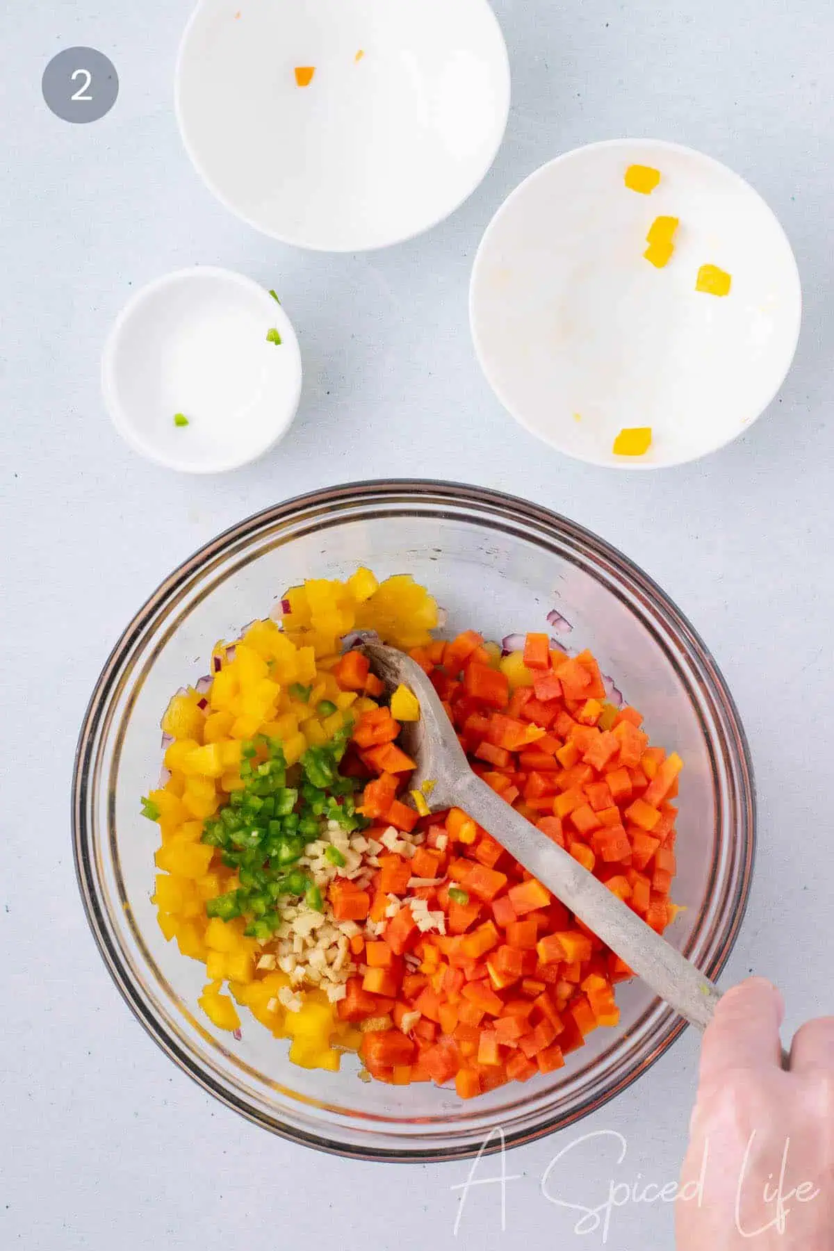 diced mango papaya pineapple and jalapeno being gently mixed in a bowl for fresh fruit salsa