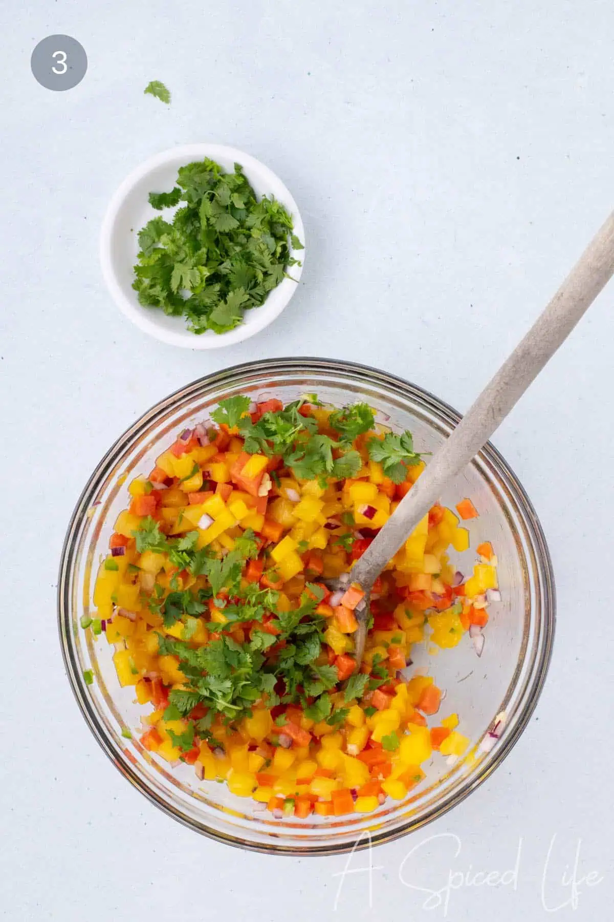 fresh cilantro being added to mango papaya salsa in a bowl before serving