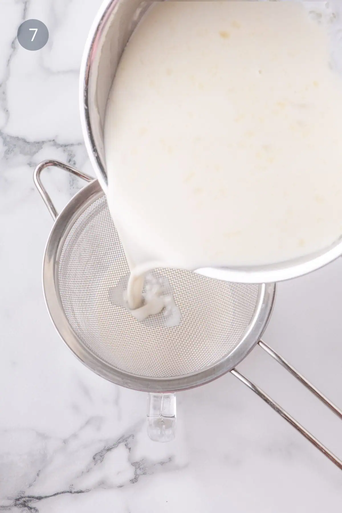 Straining coconut panna cotta mixture through fine mesh sieve.