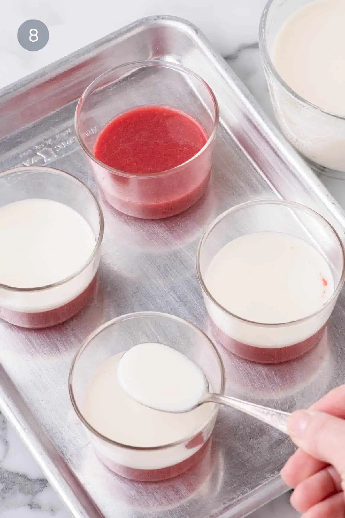 Layering coconut panna cotta over strawberry base in dessert glasses.