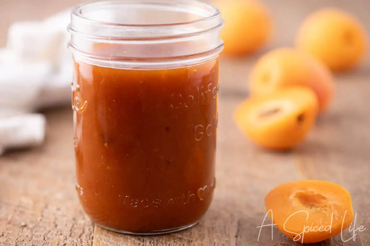 Jar of homemade apricot barbecue sauce on a wooden table with fresh apricots