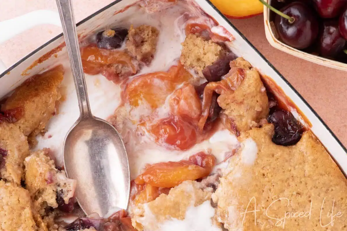 Cherry peach cobbler with melting vanilla ice cream showing the juicy fruit filling and tender cobbler topping.