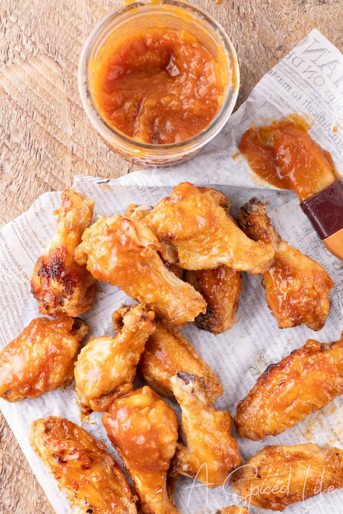Spread of chicken wings on newspaper with a jar of apricot barbecue sauce.