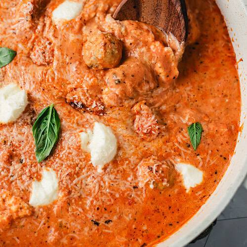 Wooden spoon lifting a chicken ricotta meatball from creamy fire-roasted tomato sauce with Parmesan and basil.