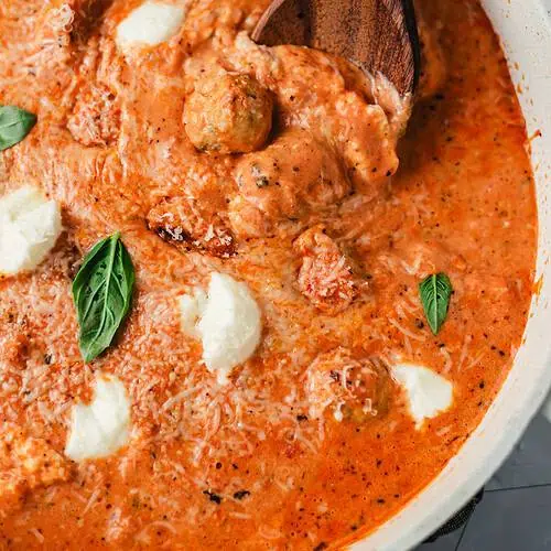 Wooden spoon lifting a chicken ricotta meatball from creamy fire-roasted tomato sauce with Parmesan and basil.