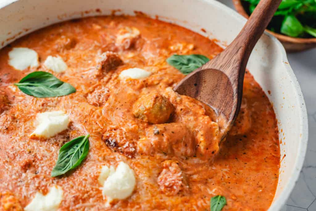 Close-up of chicken meatballs with ricotta cheese in a creamy tomato sauce garnished with fresh basil.
