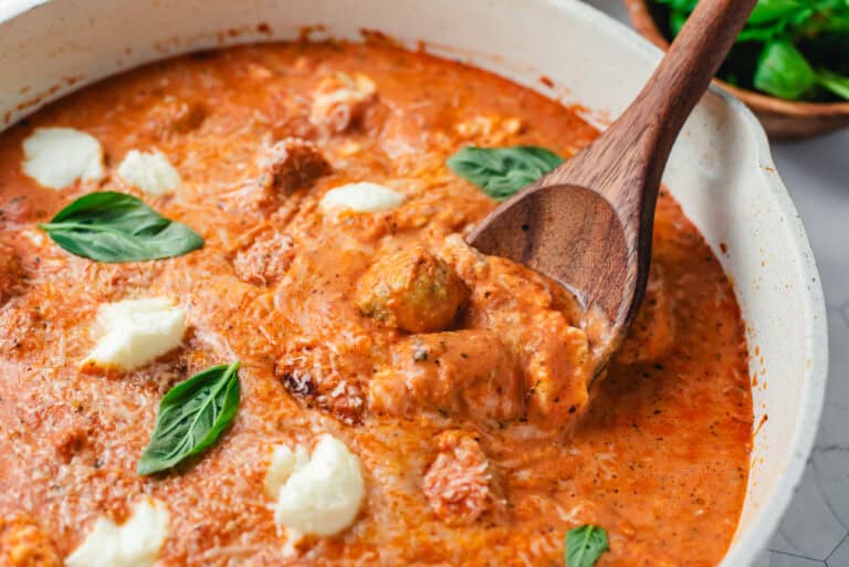 Close-up of chicken meatballs with ricotta cheese in a creamy tomato sauce garnished with fresh basil.