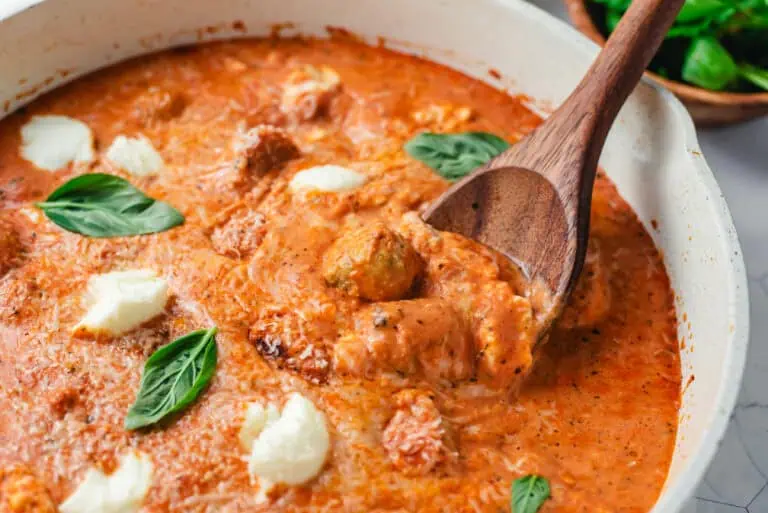 Close-up of chicken meatballs with ricotta cheese in a creamy tomato sauce garnished with fresh basil.