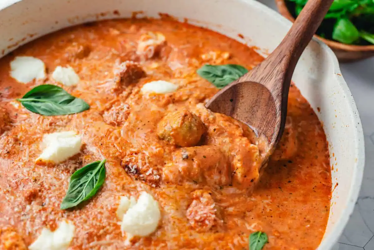 Close-up of chicken meatballs with ricotta cheese in a creamy tomato sauce garnished with fresh basil.