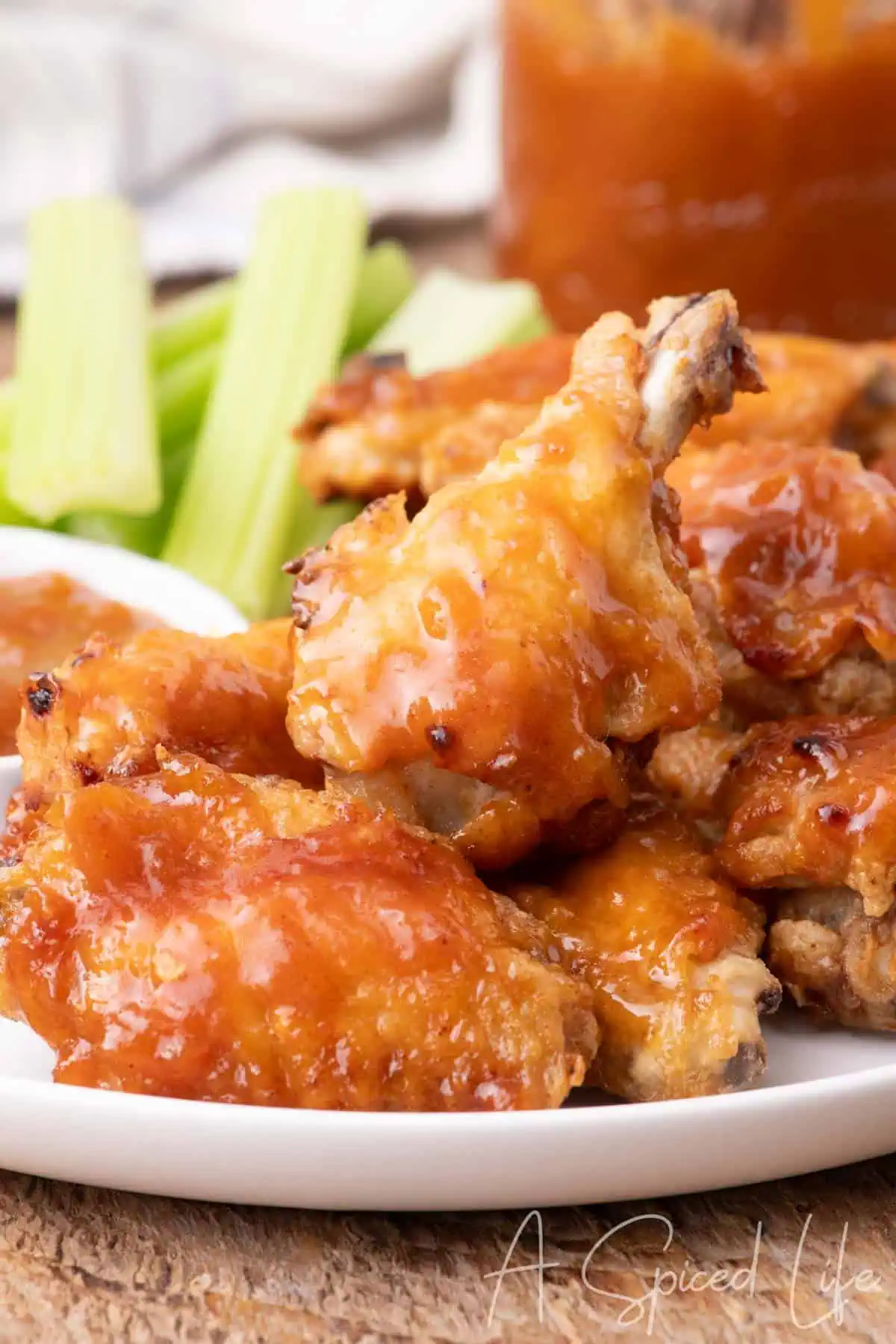 Apricot barbecue sauce coated chicken wings piled high on a plate with celery sticks in the background