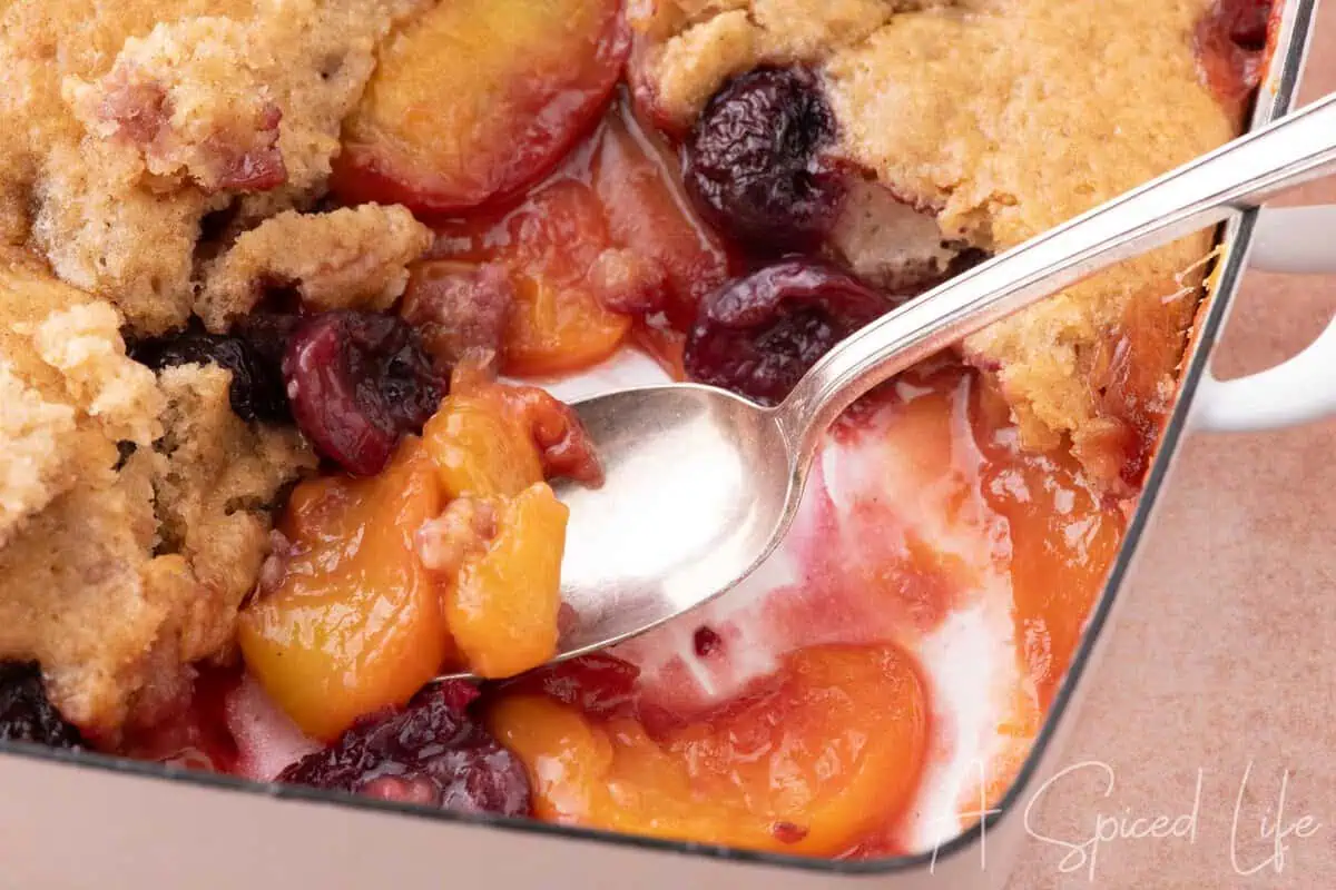 Close-up of homemade cherry peach cobbler with peaches and cherries beneath a golden topping.