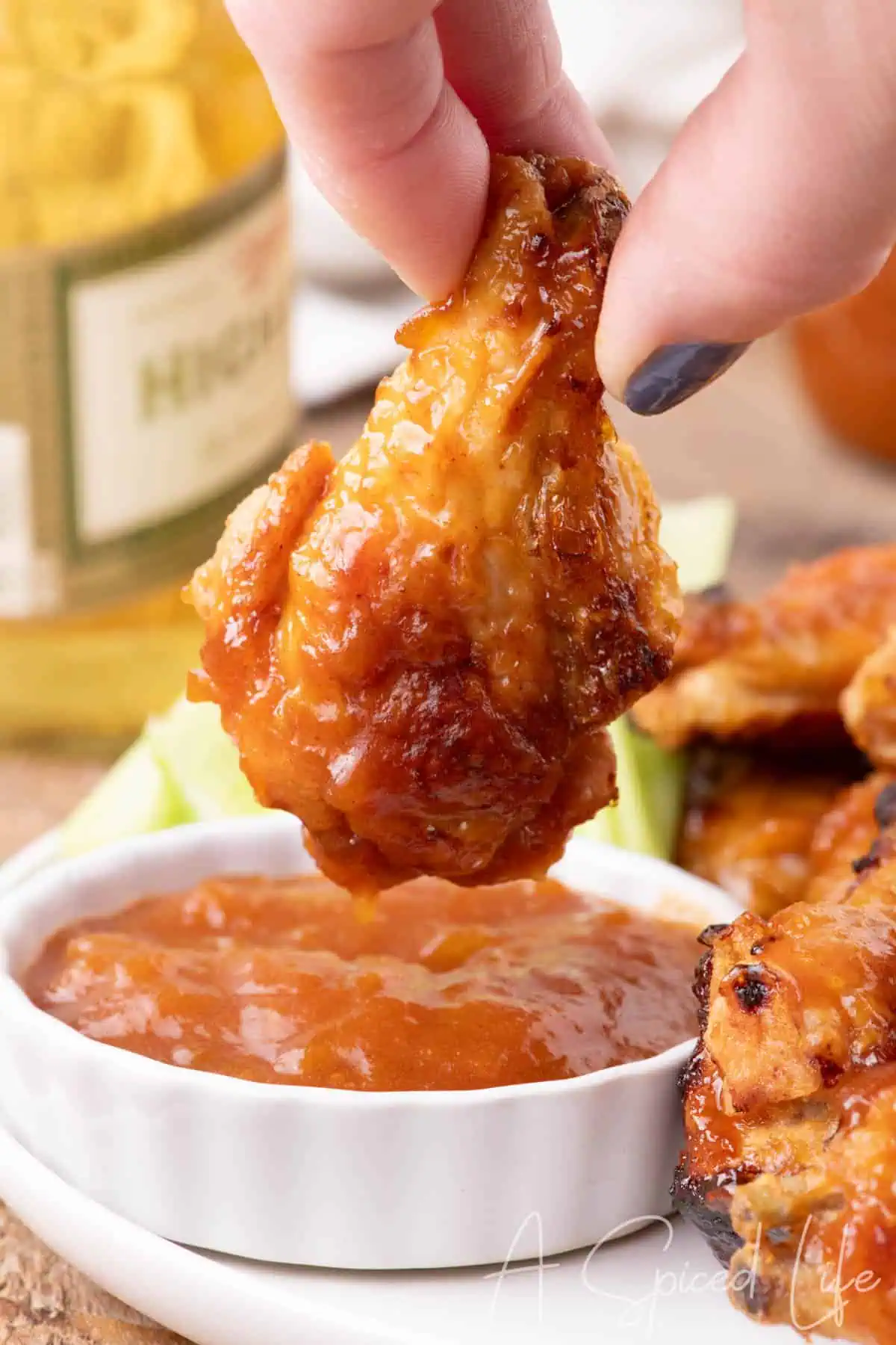 Crispy chicken wing being dipped into a jar of Apricot Barbecue Sauce