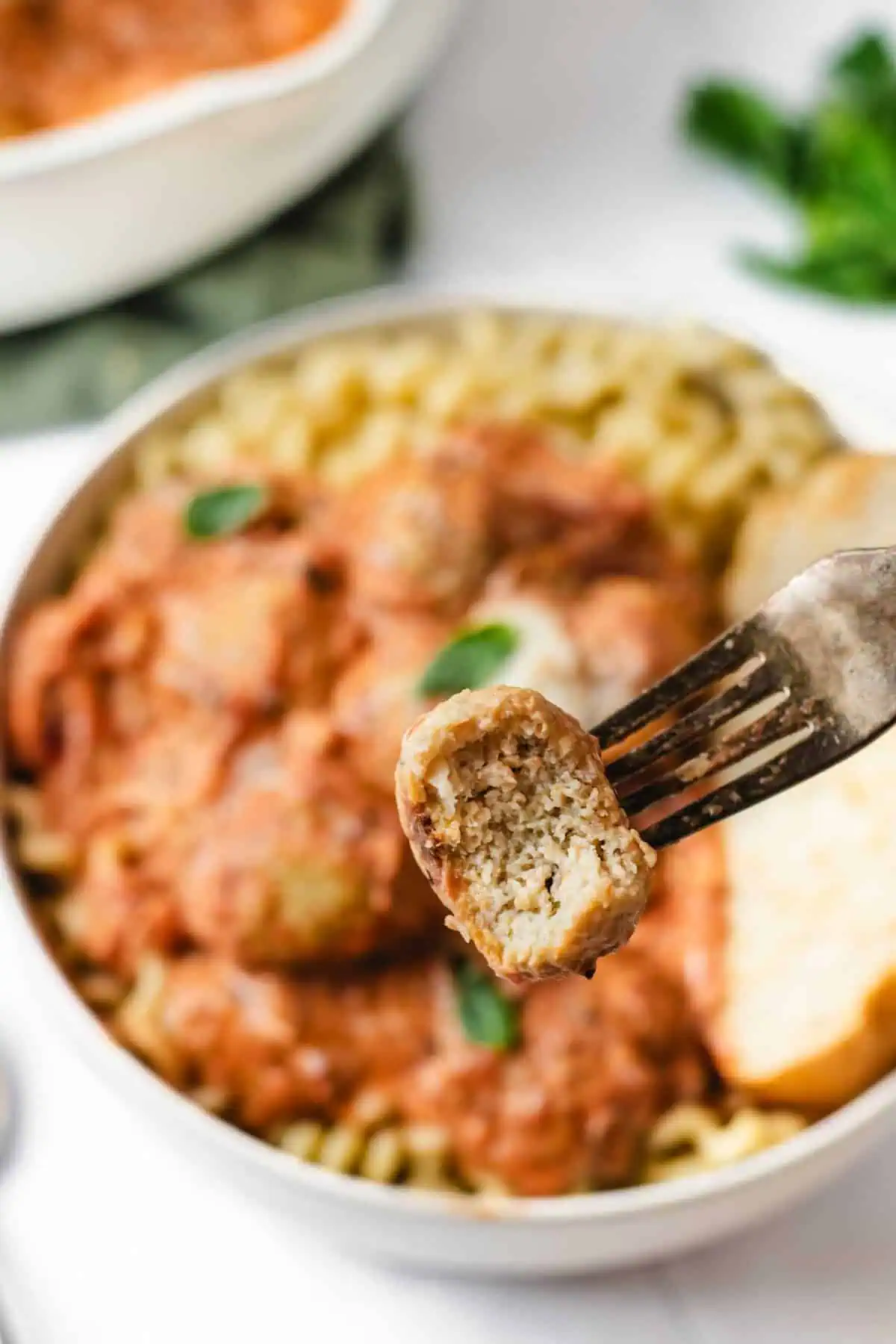 Fork holding a tender chicken and ricotta meatball showing the moist interior above a bowl of pasta and creamy tomato sauce.