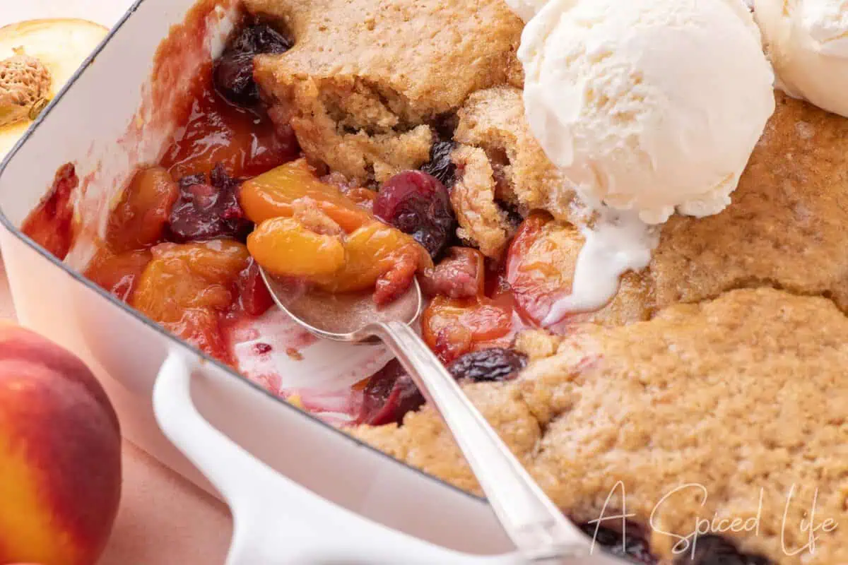 Summer cherry and peach cobbler served warm with melting vanilla ice cream.
