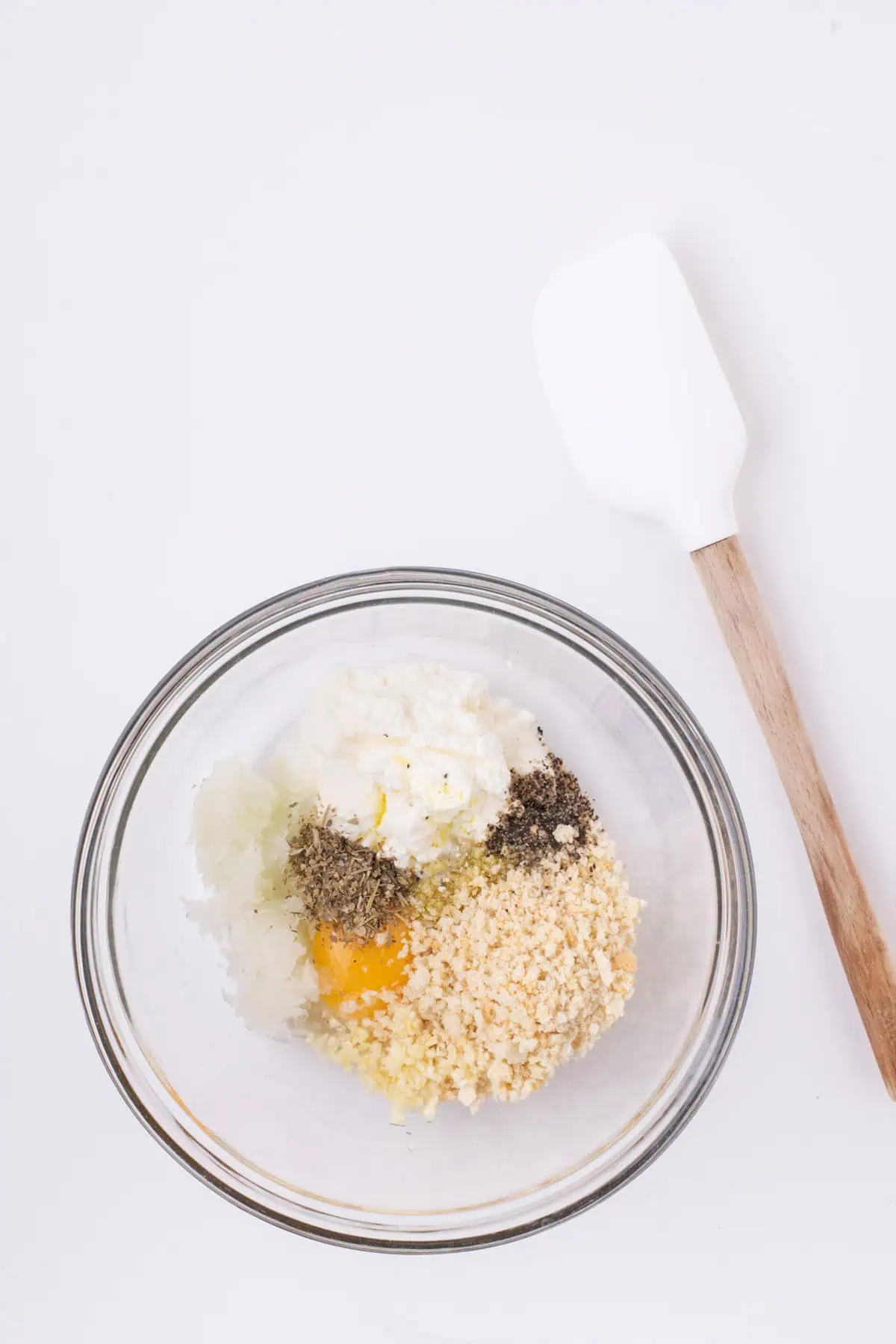 Ricotta, panko, egg, grated onion, garlic, Parmesan, and seasonings in a glass mixing bowl.