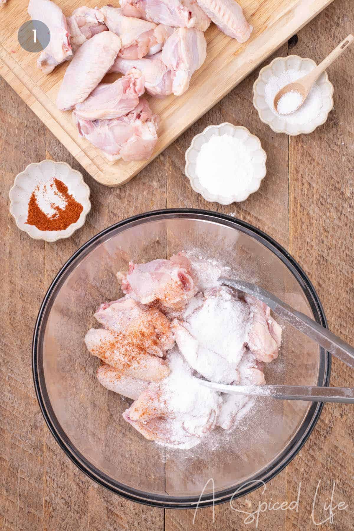 Chicken wings tossed with baking powder, salt, and cayenne pepper in a mixing bowl.