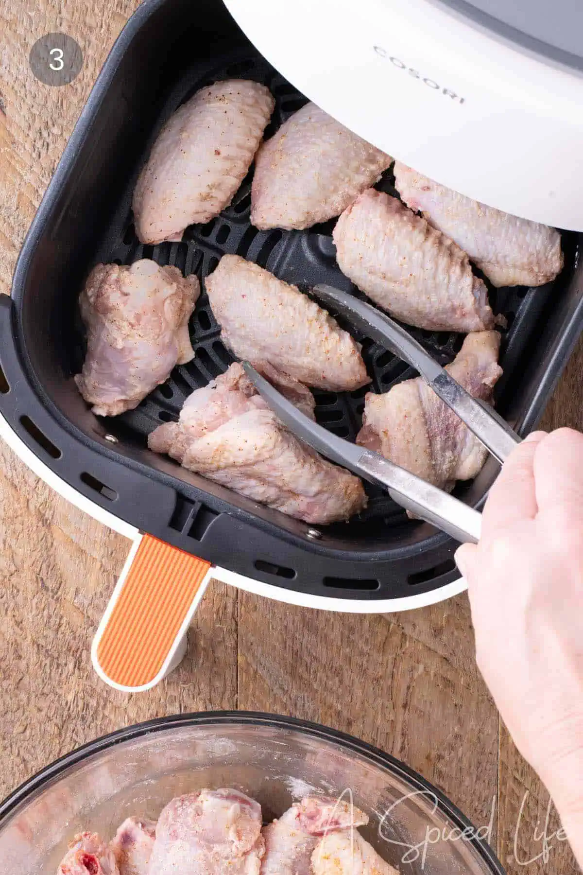 Seasoned chicken wings arranged in an air fryer basket before cooking.