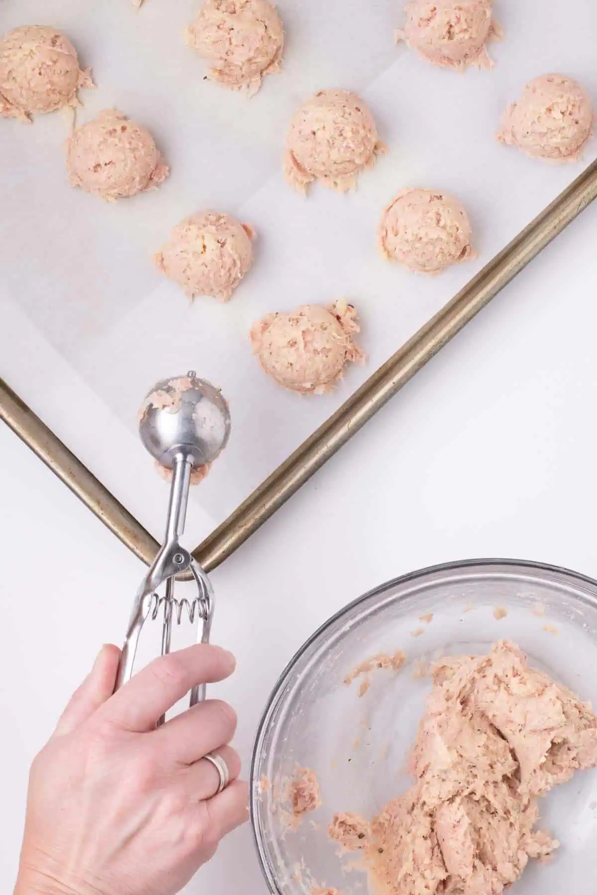 Chicken meatball mixture being scooped onto a parchment-lined baking sheet.