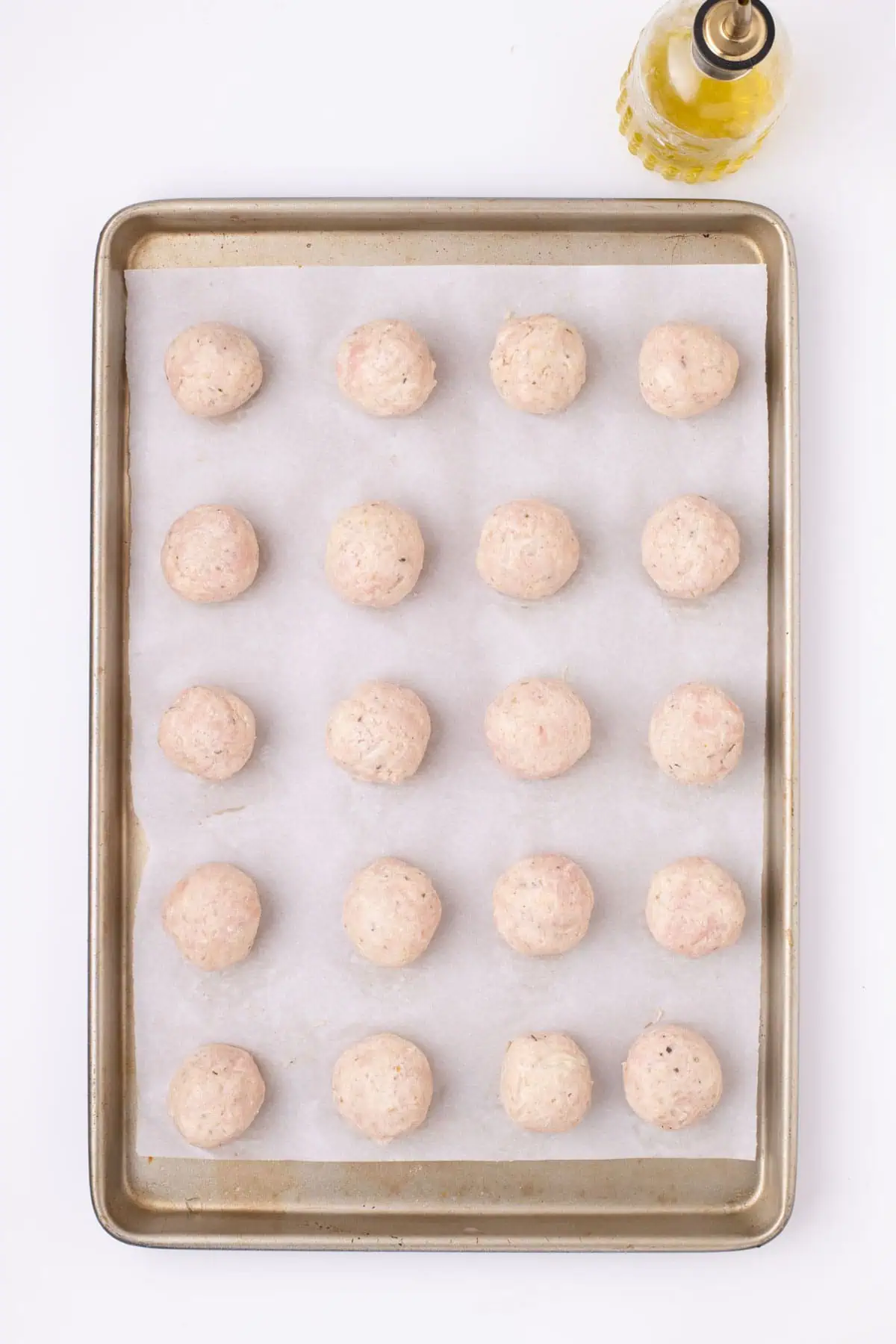 Raw chicken meatballs arranged on a parchment-lined baking sheet before baking.