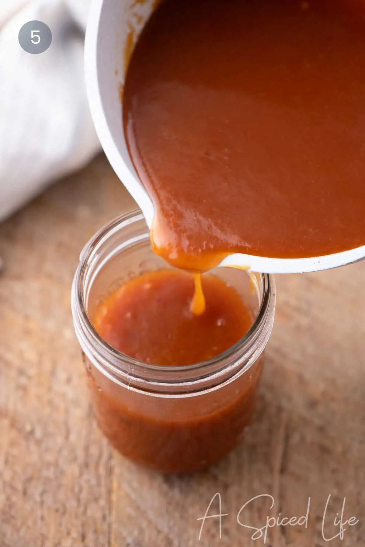 Pouring homemade apricot BBQ sauce into a glass jar for storage