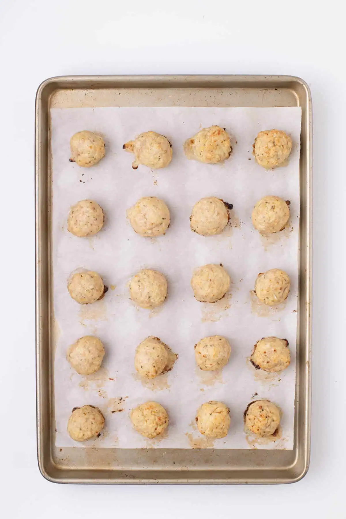 Baked chicken meatballs on a parchment-lined baking sheet.