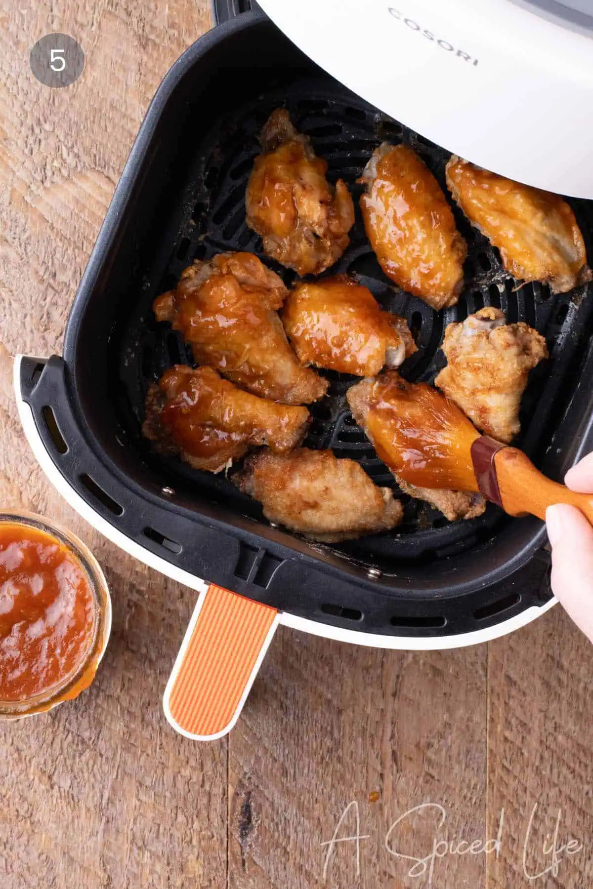 Brushing apricot bourbon barbecue sauce onto crispy air fryer chicken wings.