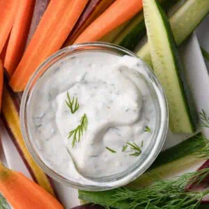 Creamy yogurt dip with fresh dill and colorful vegetables in the background