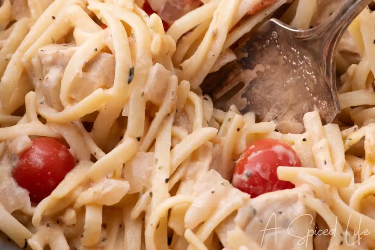 Close-up of creamy slow cooker chicken spaghetti with tender chicken, cherry tomatoes, and pasta.