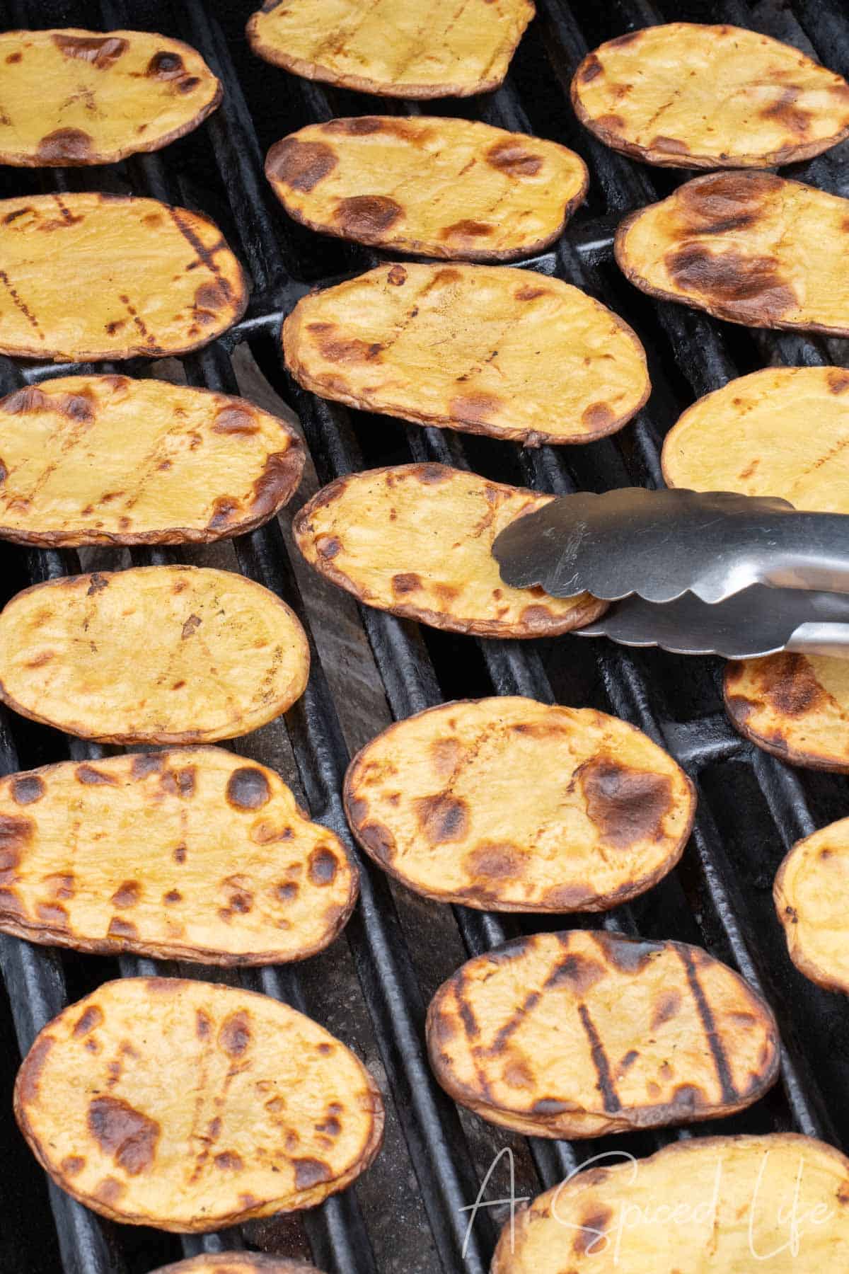 Grilled potato slices with golden edges cooking on an outdoor grill.